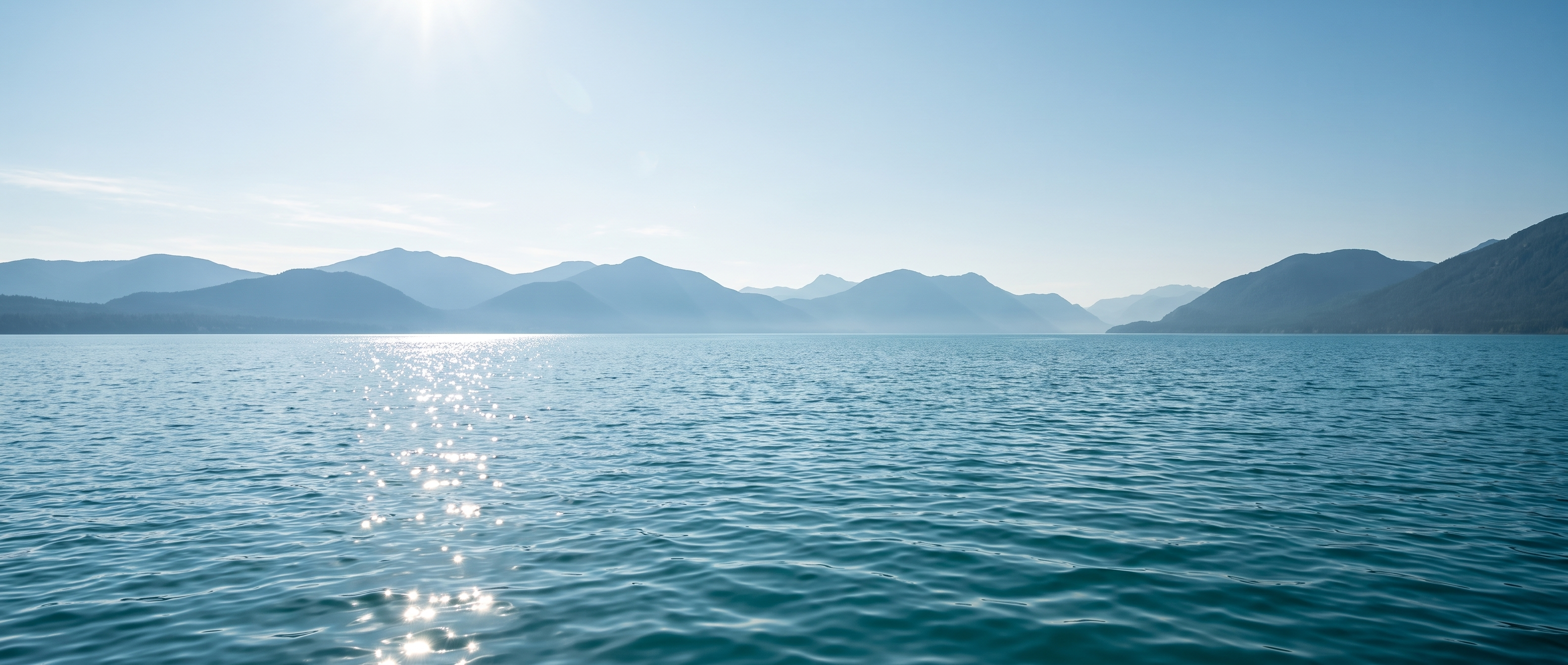 Sunlight sparkling across a blue-green lake beneath distant mountains